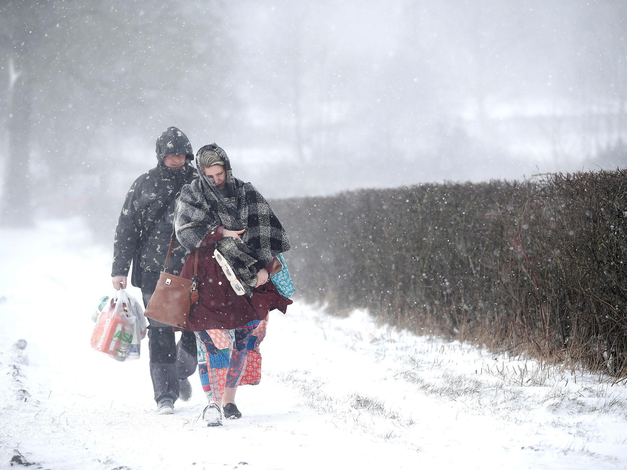 A couple walk along the A53 Buxton Road, which is closed due to heavy snow fall, after abandoning their car near Leek