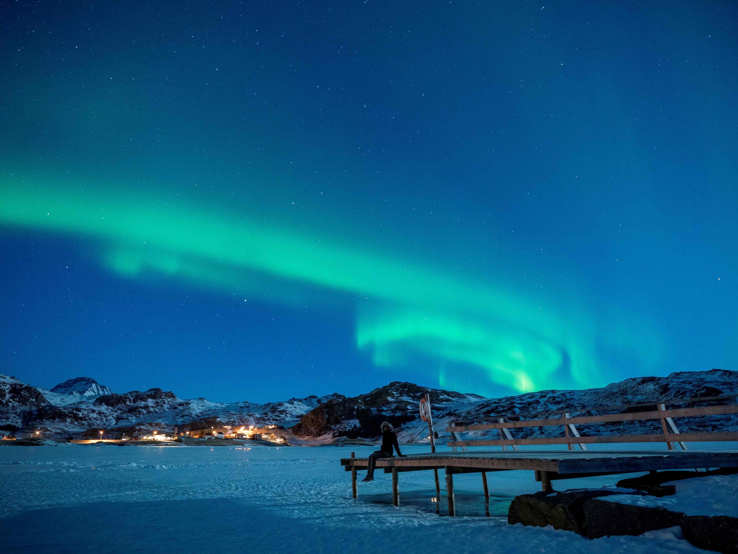 A woman sits on a pier to watch northern lights on the Lofoten Islands, in Bostad, in the arctic circle in northern Norway