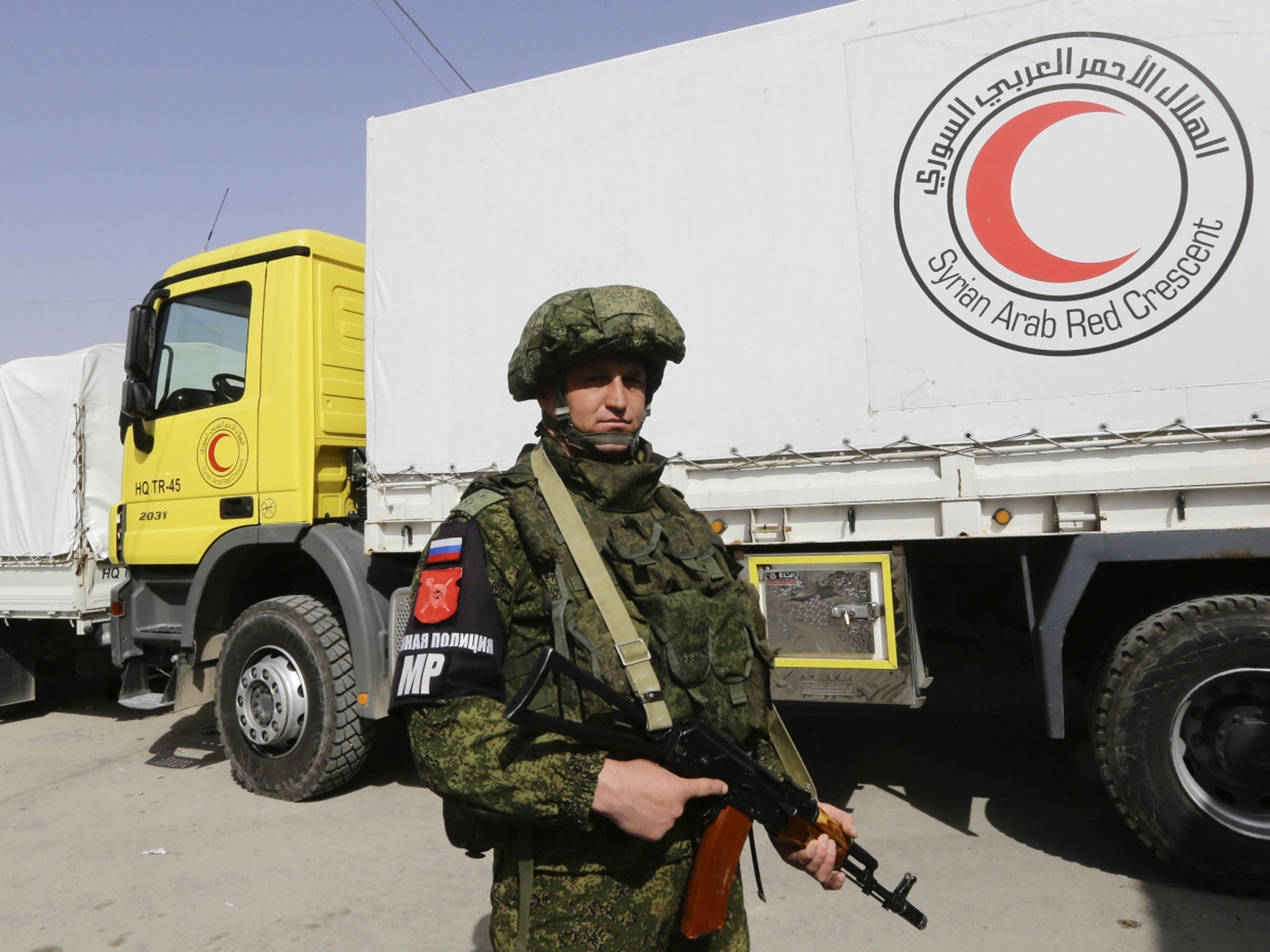 A Russian soldier stands guard as Syrian Arab Red Crescent vehicles carrying aid wait to enter Eastern Ghouta
