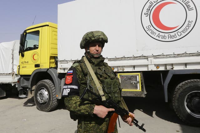 A Russian soldier stands guard as Syrian Arab Red Crescent vehicles carrying aid wait to enter Eastern Ghouta