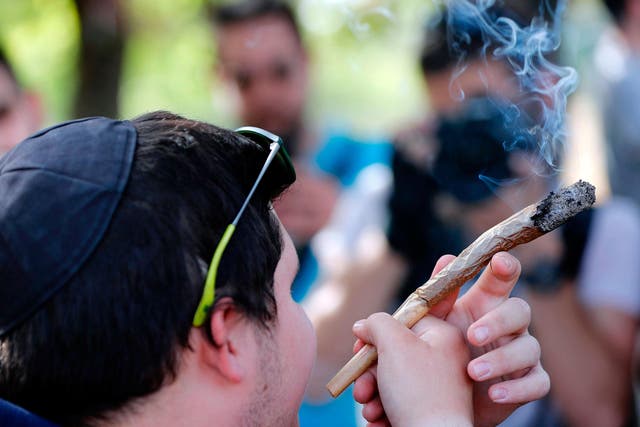 An Israeli man smokes a giant marijuana joint during a rally to celebrate '420' in the Rose garden, just across from the Knesset
