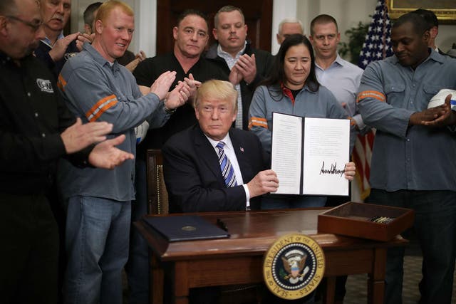 Surrounded by steel and aluminium workers, President Donald Trump holds up the  ‘Section 232 Proclamations’ on steel imports that he signed at the White House