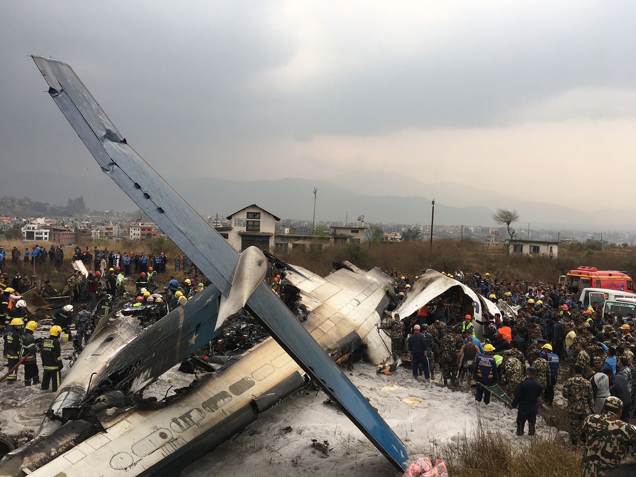 Nepalese rescuers stand near a passenger plane from Bangladesh that crashed at the airport in Kathmandu