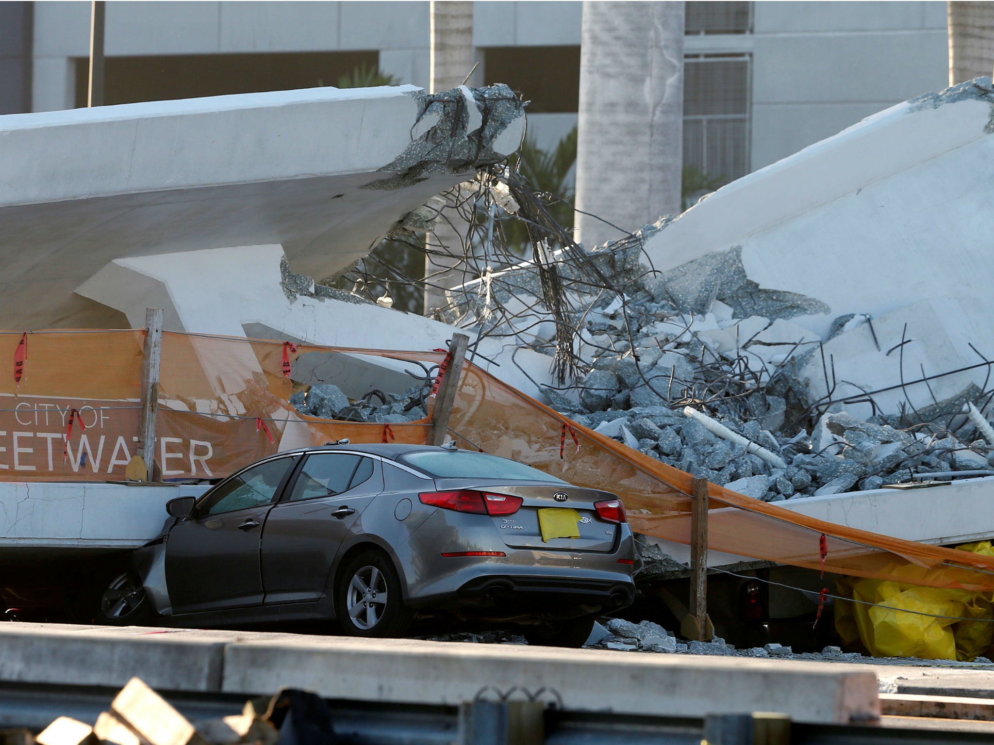 A damaged car partially crushed under a collapsed pedestrian bridge near Florida International University in Miami