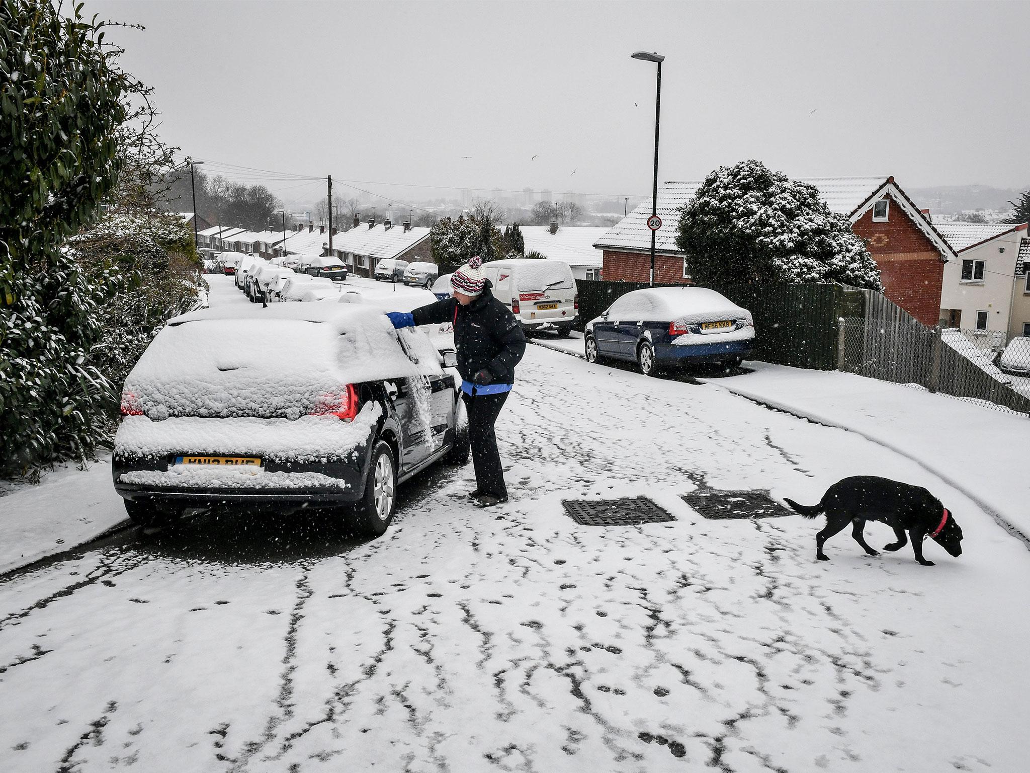 A woman clears snow off a car in Bristol after snow on Saturday