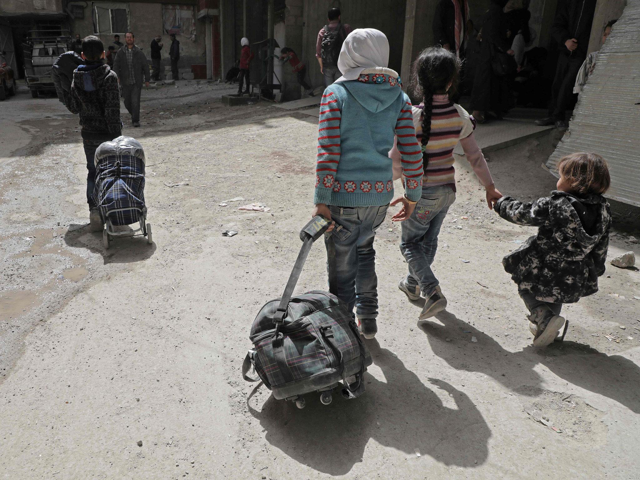 Syrian children walk with their luggage as they wait for their evacuation by the Syrian Red Crescent in the rebel-held Eastern Ghouta enclave on Thursday