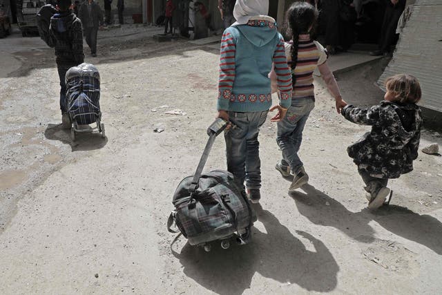 Syrian children walk with their luggage as they wait for their evacuation by the Syrian Red Crescent in the rebel-held Eastern Ghouta enclave on Thursday