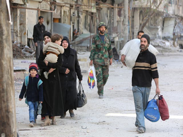 Syrian people walk down a street past a destroyed building as civilians and rebels prepare to evacuate the town of Ain Tarma in the eastern Ghouta region near Damascus on March 25, 2018