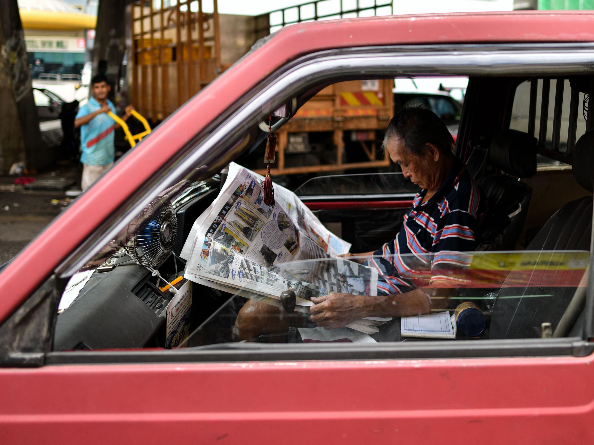 A Malaysian man with a newspaper on his lap inside his minivan at a wet market in downtown Kuala Lumpur on January 18, 2018