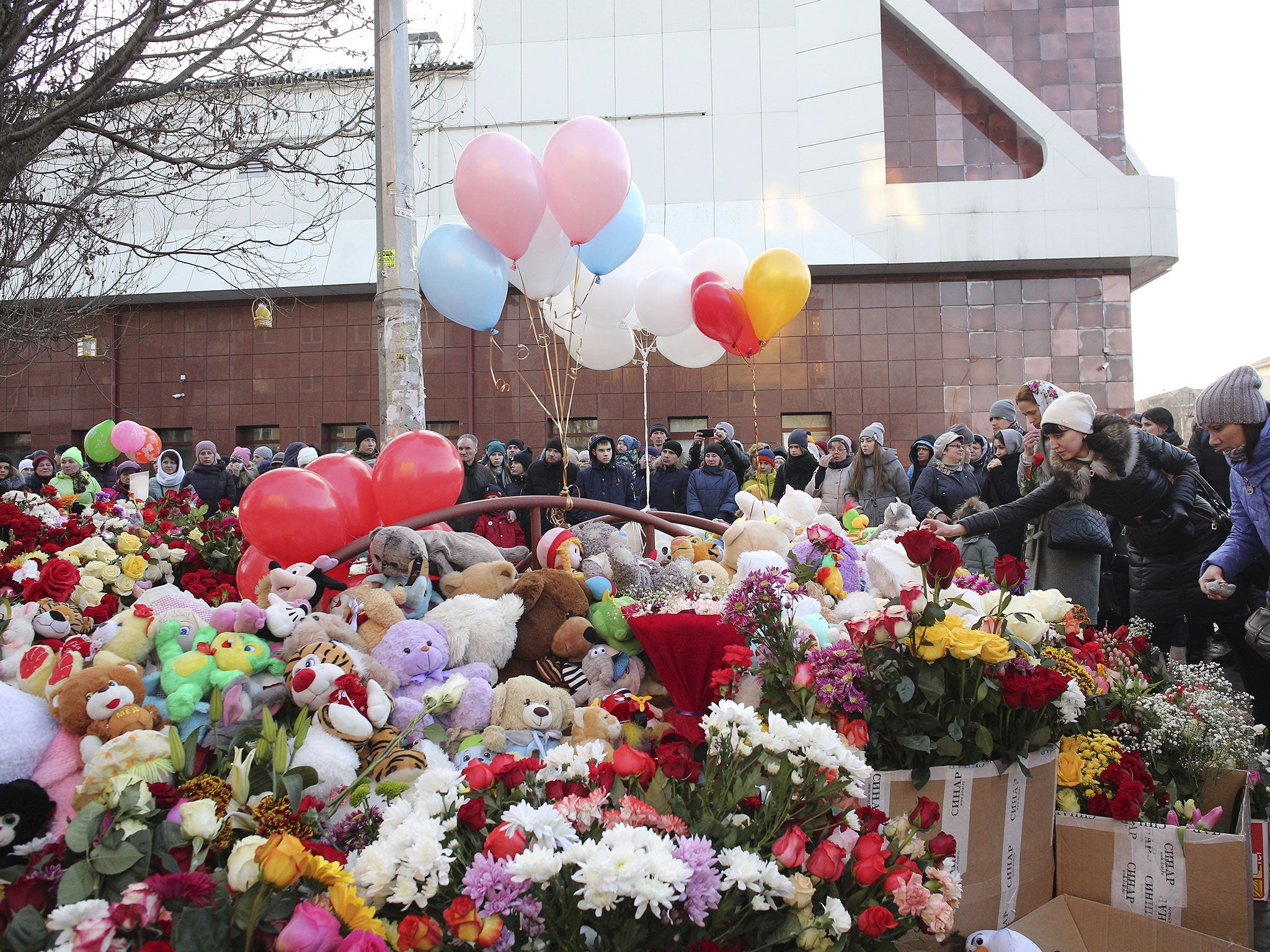 People lay flowers for the victims of the fire in a multi-story shopping centre with the mall in the background