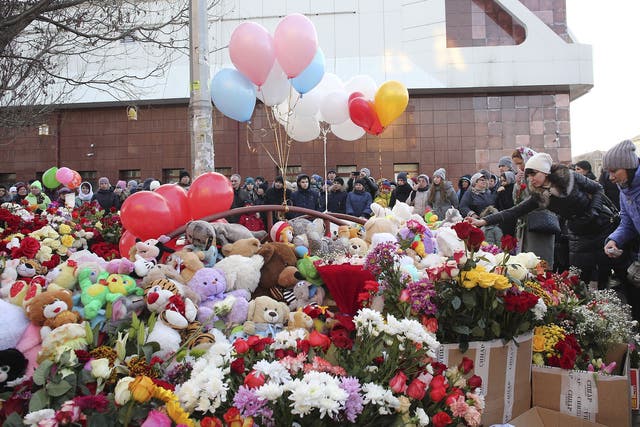 People lay flowers for the victims of the fire in a multi-story shopping center with the mall in the background