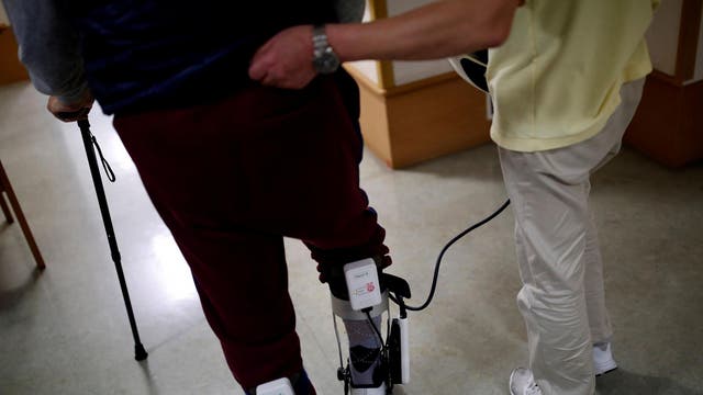 A caretaker, wearing walking rehabilitation equipment 'Tree', helps a resident with his walking training at Shin-tomi nursing home in Tokyo, Japan