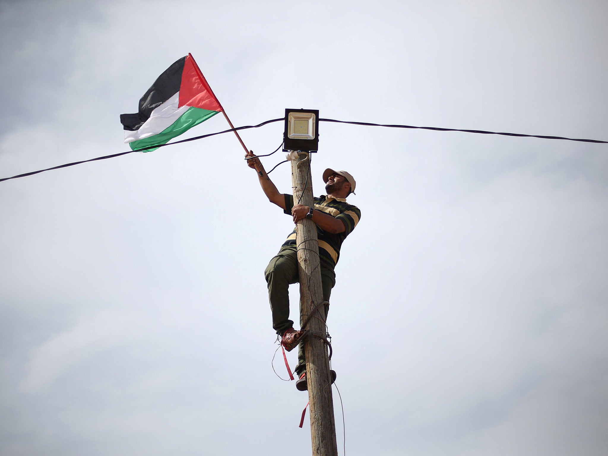 A man hangs a Palestinian flag at an electric pole