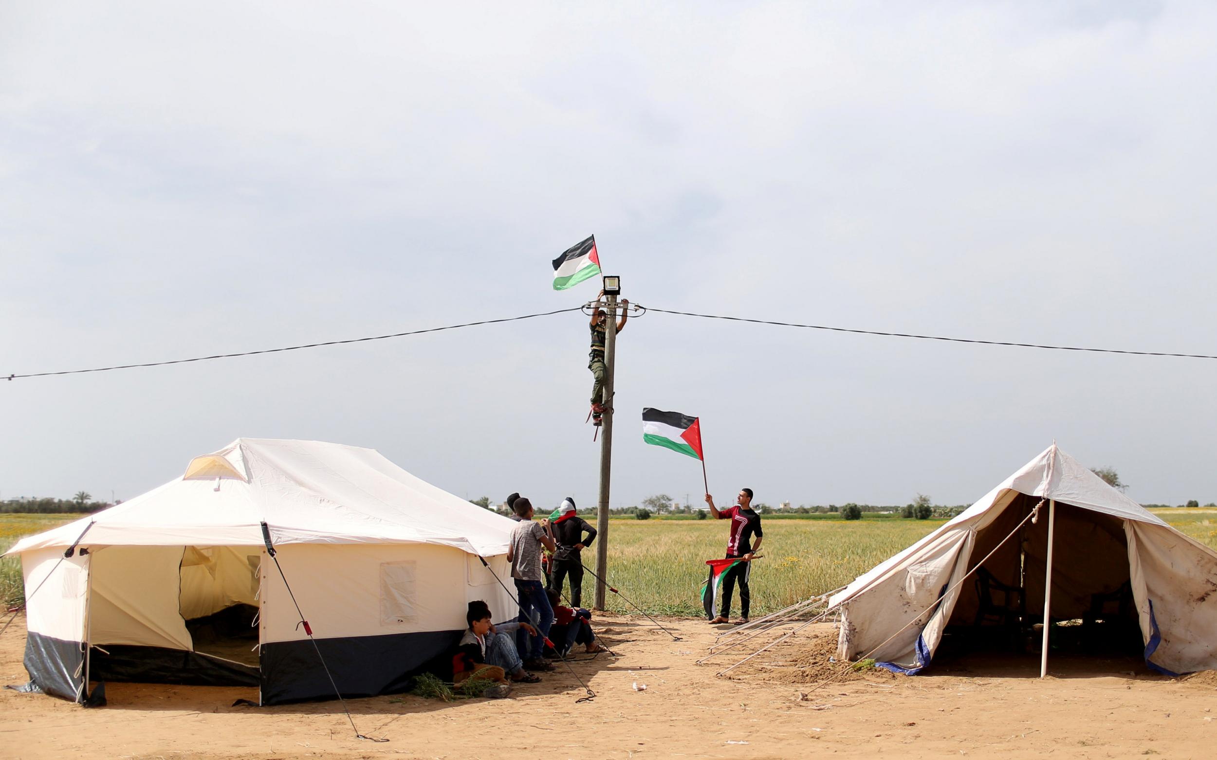 A man hangs a Palestinian flag amid a collection of tents near the border with Israel, in the southern Gaza Strip
