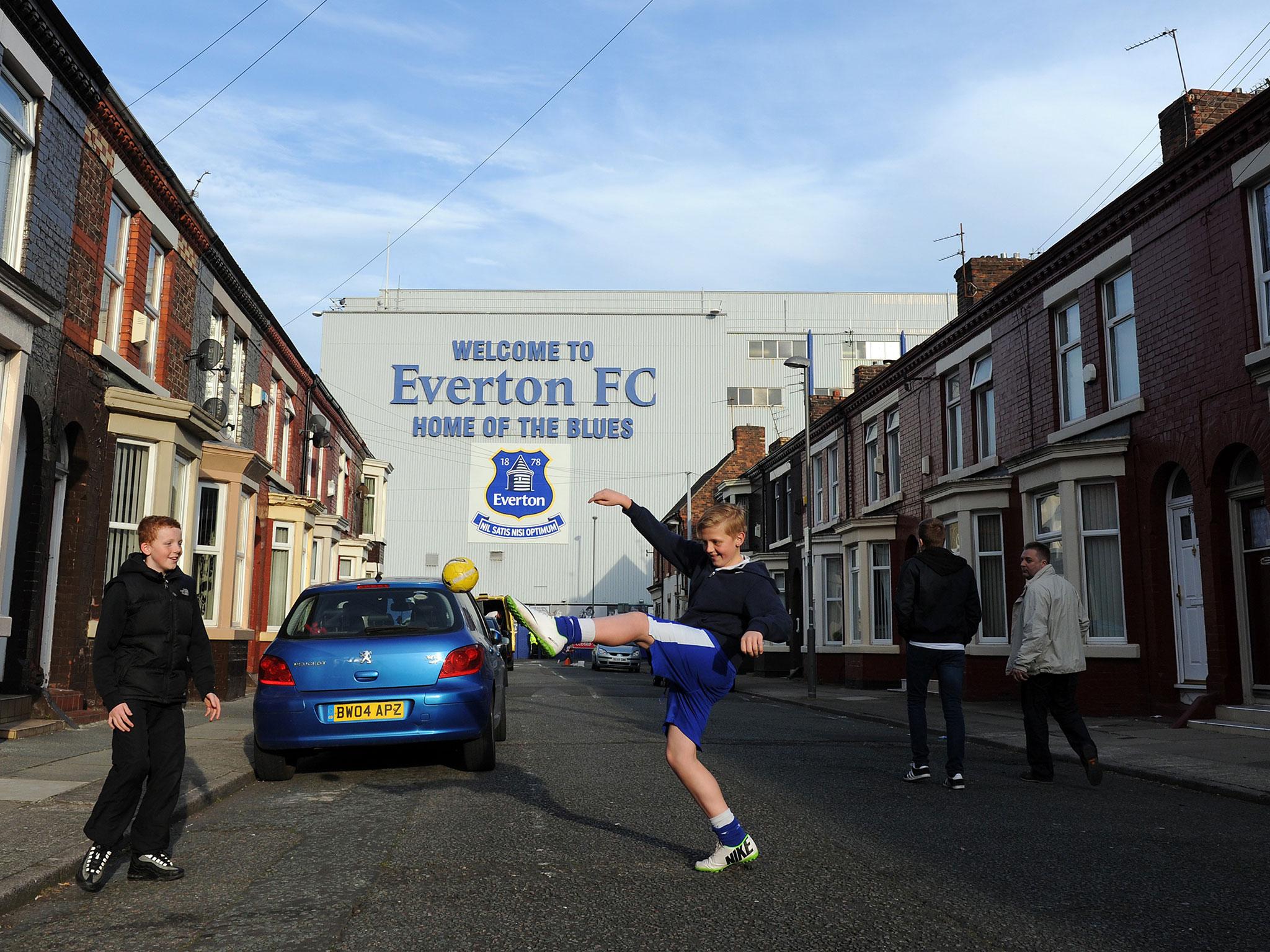 Two children knock a ball about in the shadow of Goodison Park