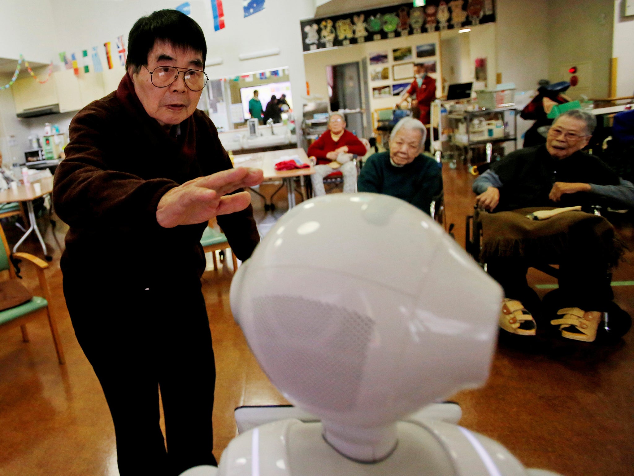 A resident approaches humanoid robot 'Pepper' to pat its head during an afternoon exercise routine at Shin-tomi nursing home in Tokyo.
