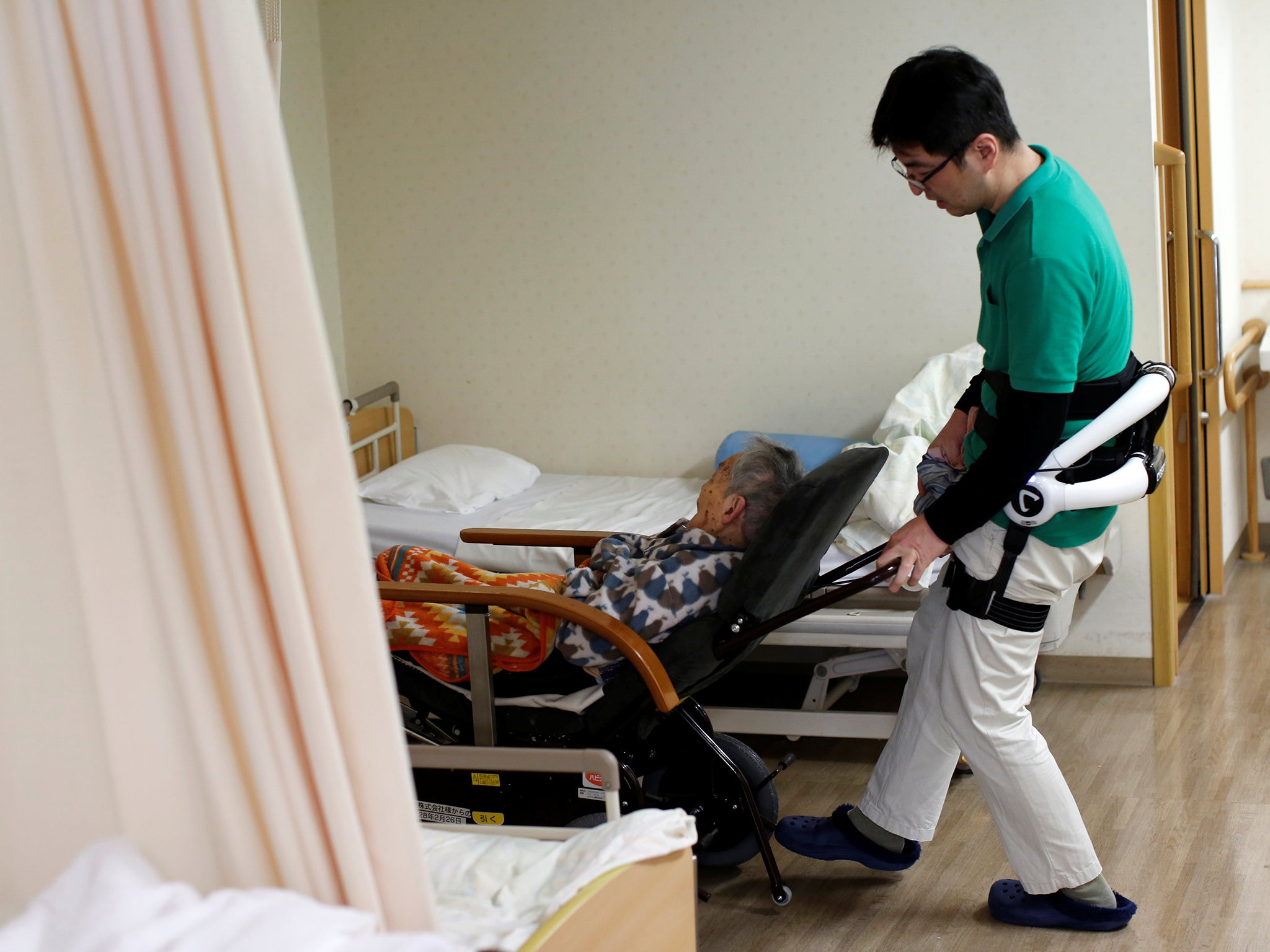 A caretaker wearing a 'HAL for care support' robot suit pushes a wheelchair at Shin-tomi nursing home in Tokyo.