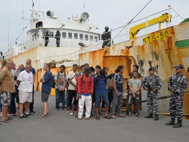 Indonesian navy soldiers hold rifles as they stand next to the detained crew of the STS-50 fishing boat at a port in Sabang, Indonesia