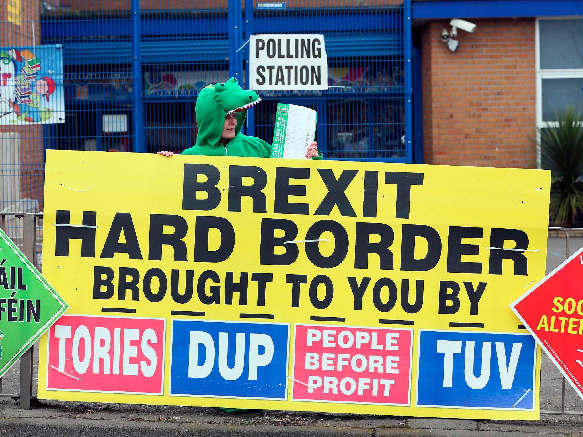 A Sinn Fein party election worker dressed up as a crocodile stands behind a banner referring to Brexit outside a polling station in Belfast