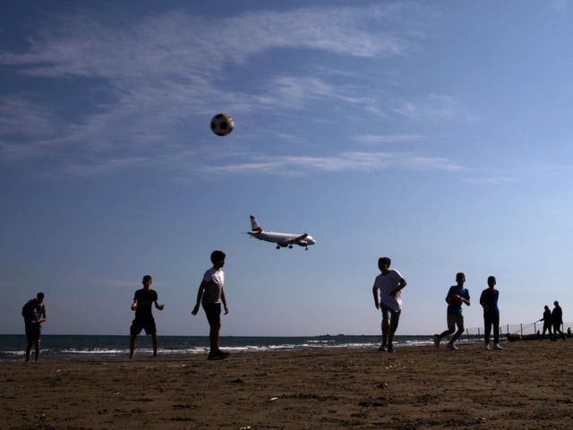 Children play football on a beach as an airplane prepares to land at Larnaca International Airport