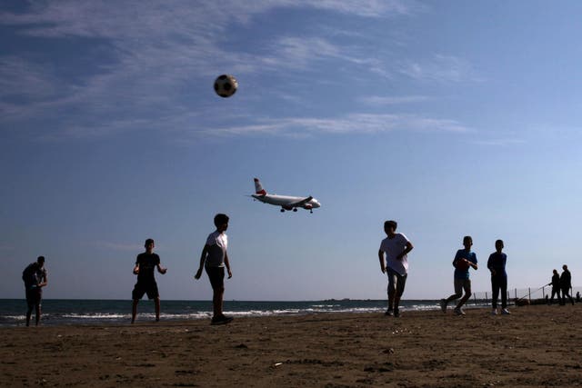 Children play football on a beach as an airplane prepares to land at Larnaca International Airport