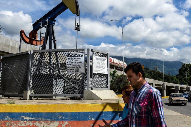 People walk by a small square with an oil pump in one of the access roads to the Central University of Venezuela, Caracas