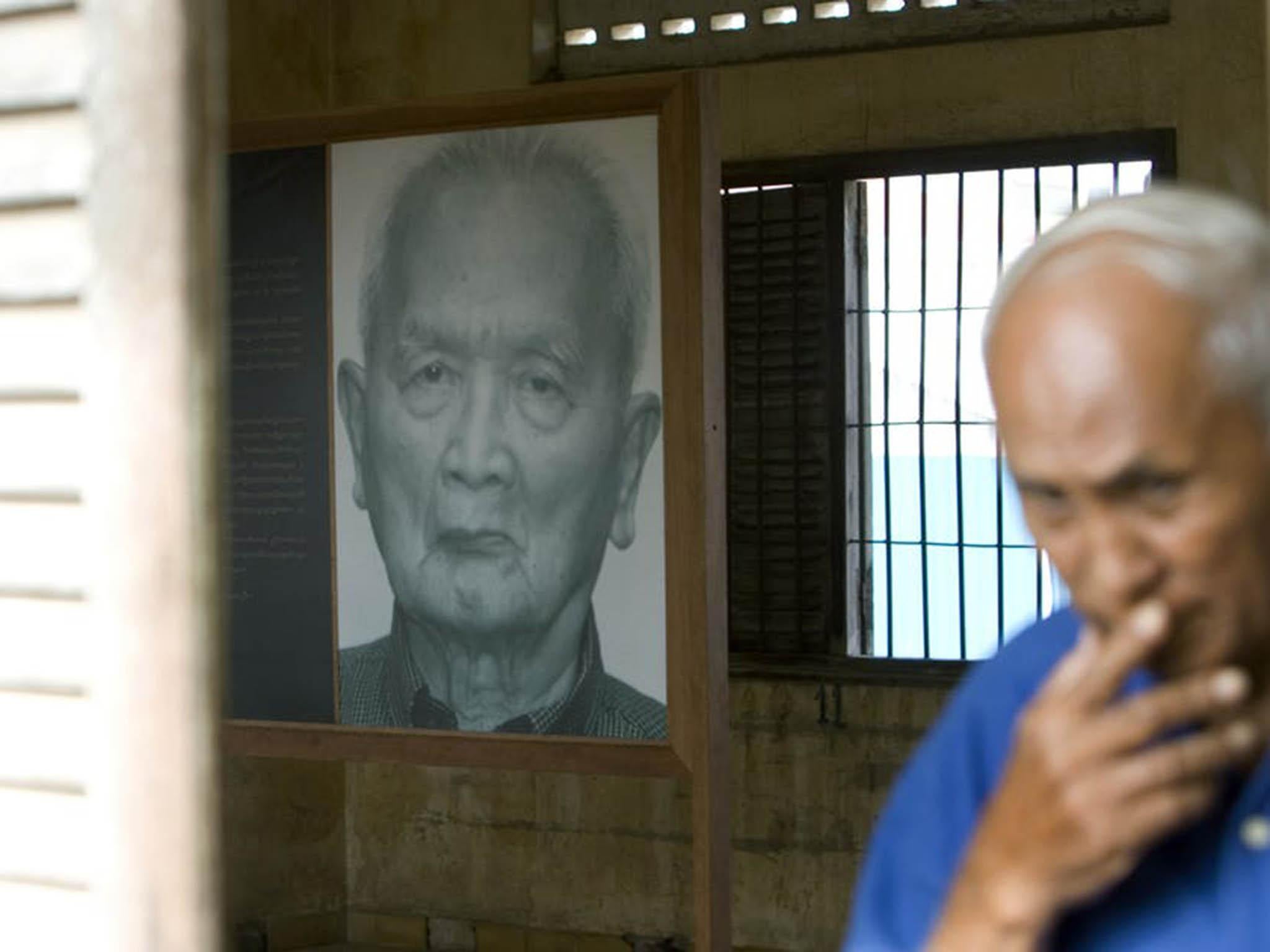 Chum Mey, a survivor of the Khmer Rouge regime, walks past a portrait of Nuon Chea, a former Khmer Rouge leader