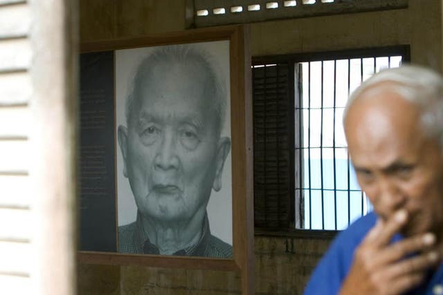 Chum Mey, a survivor of the Khmer Rouge regime, walks past a portrait of Nuon Chea, a former Khmer Rouge leader