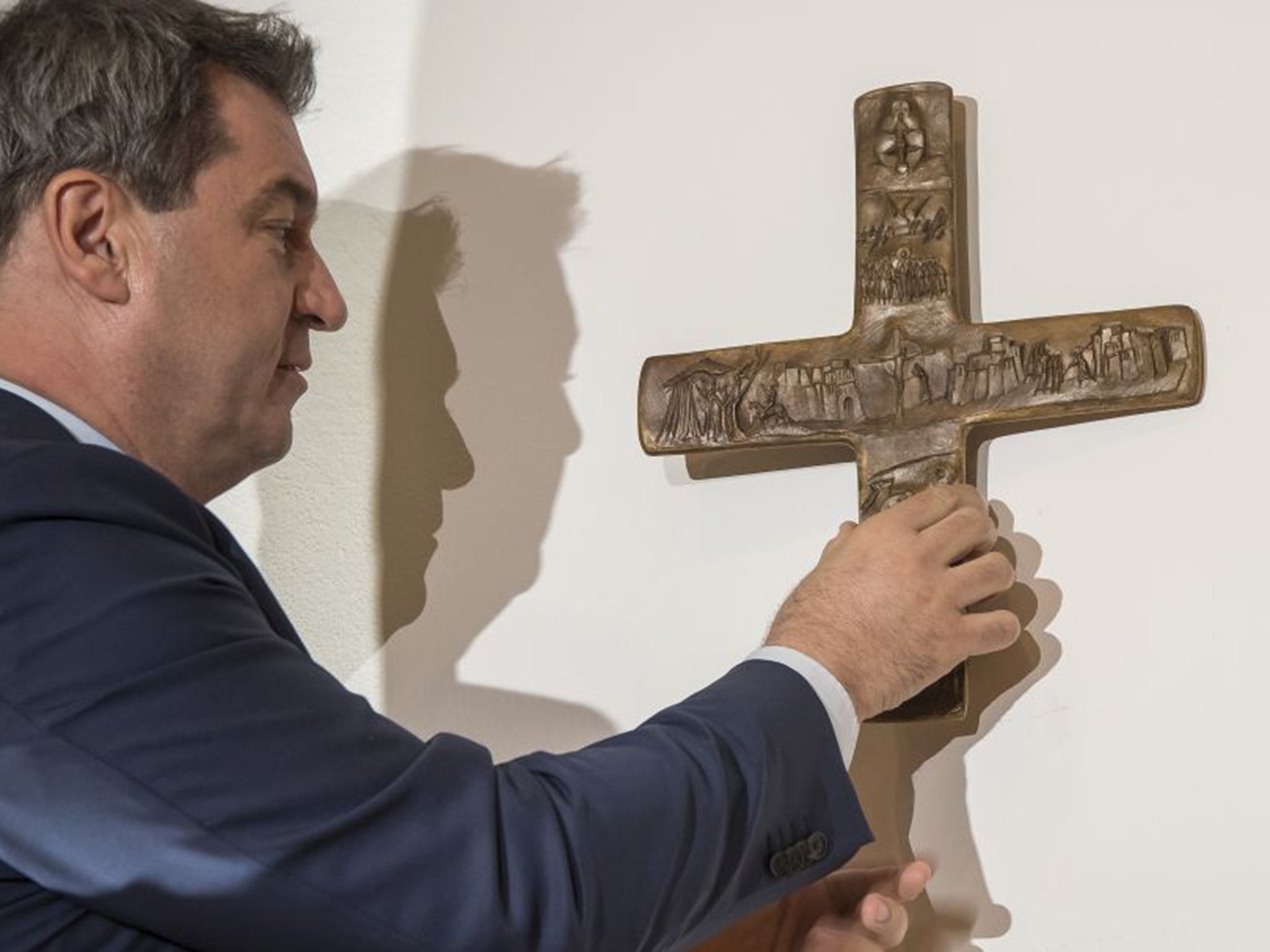 Markus Soeder, Governor of the German state of Bavaria, hangs up a cross at the entrance of the state chancellery in Munich, Germany
