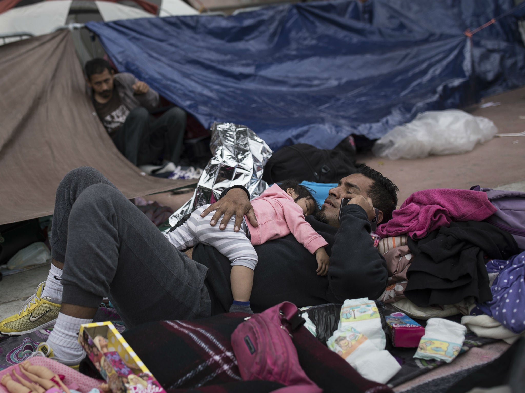 A migrant father and child rest where they set up camp to wait for access to request asylum in the US at the US-Mexico border in Tijuana, Mexico