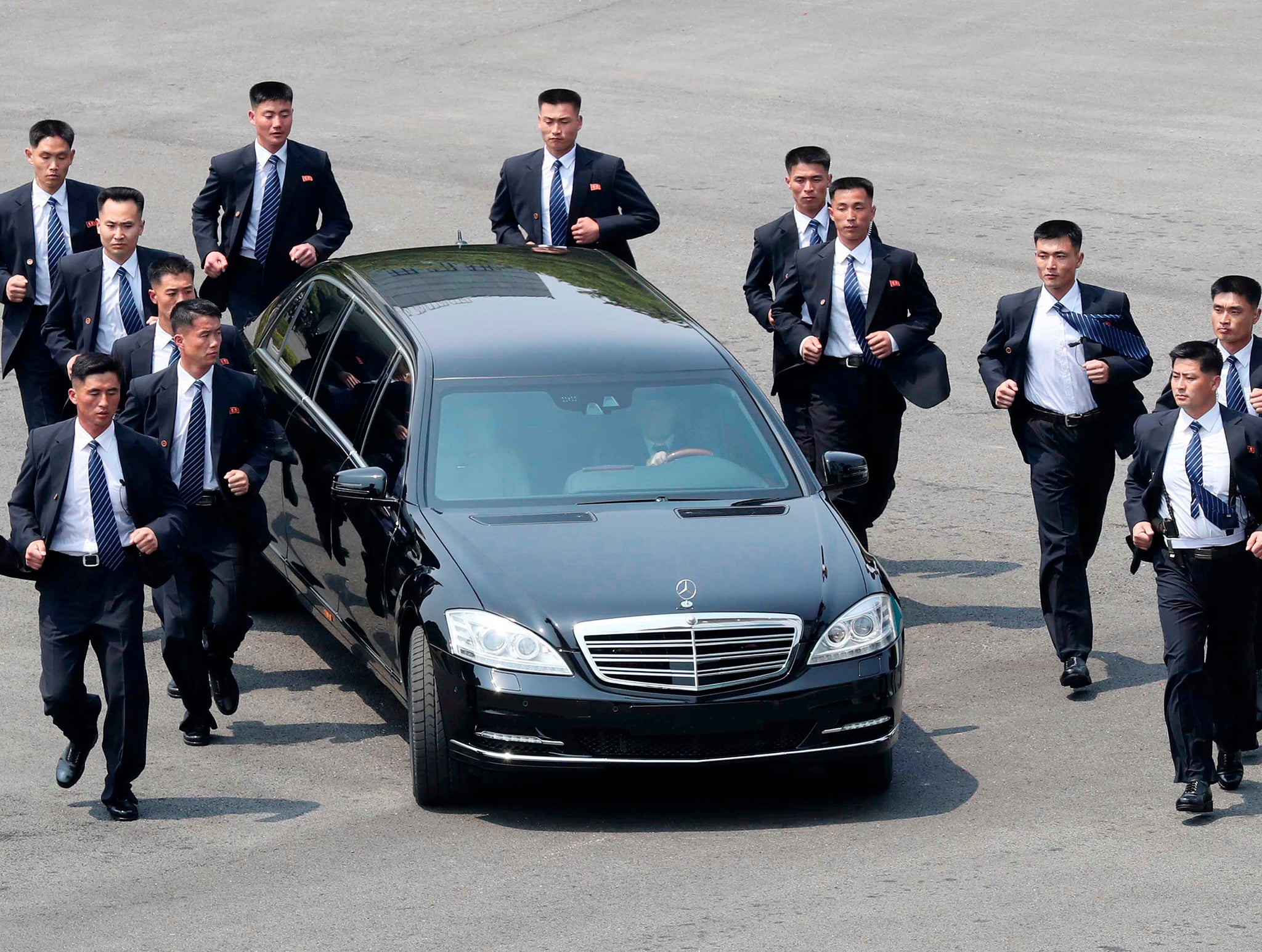 North Korean security guards run alongside a car carrying Kim Jong Un (AP Images )