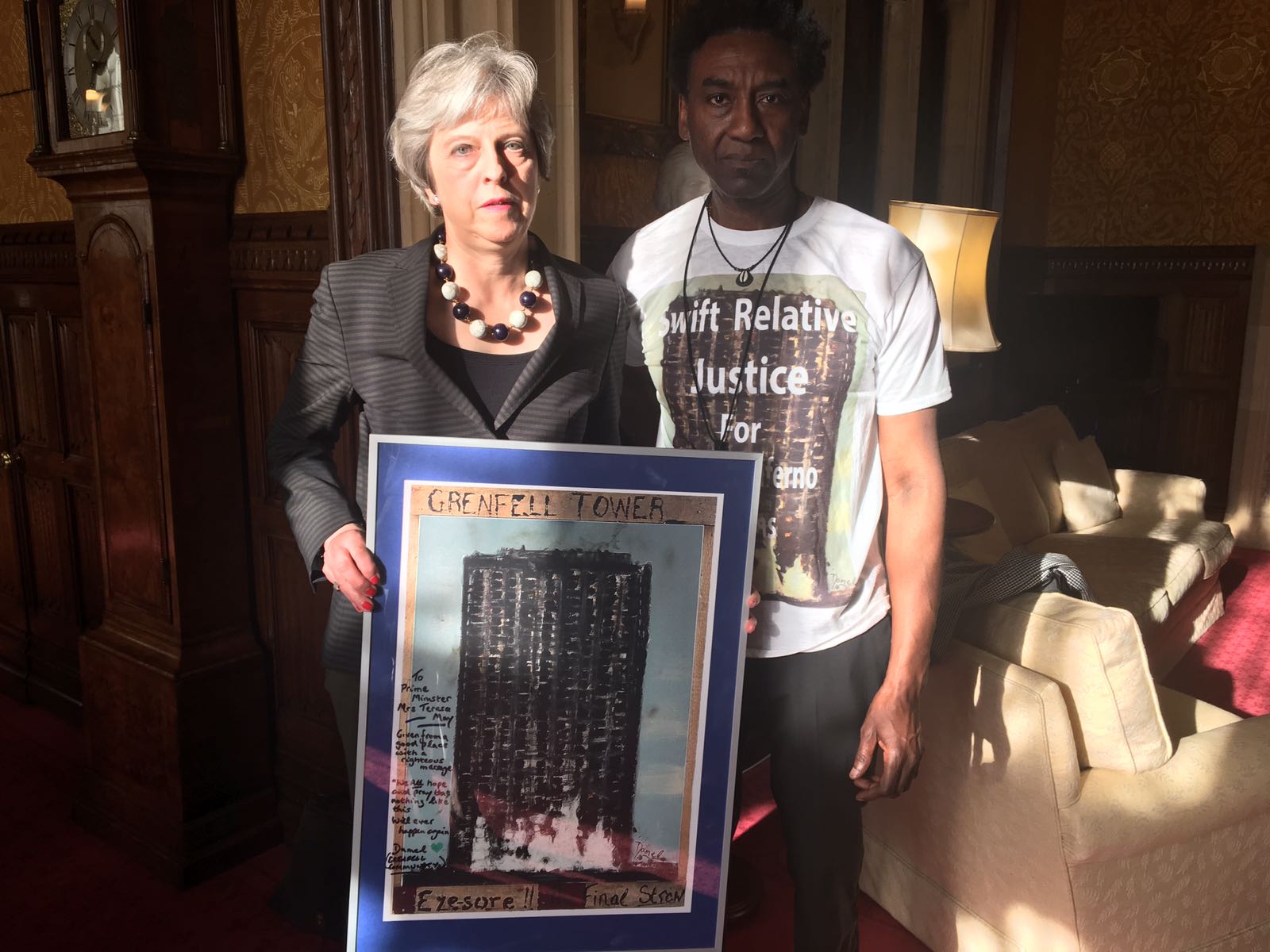 Damal Carayol, who lost relatives in the fire, stands with Theresa May as she holds up a piece of artwork he produced