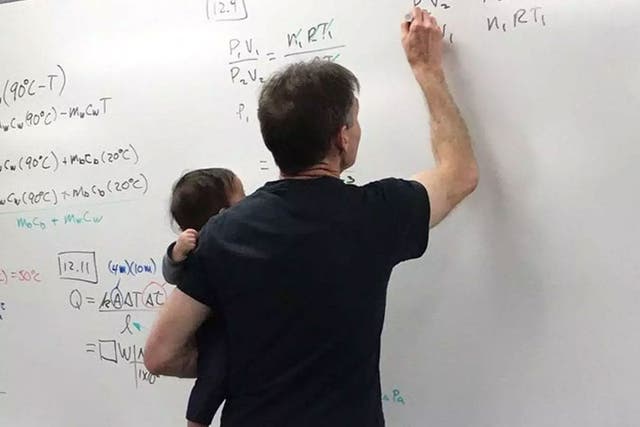 A physics lecturer holding his student's baby during a class
