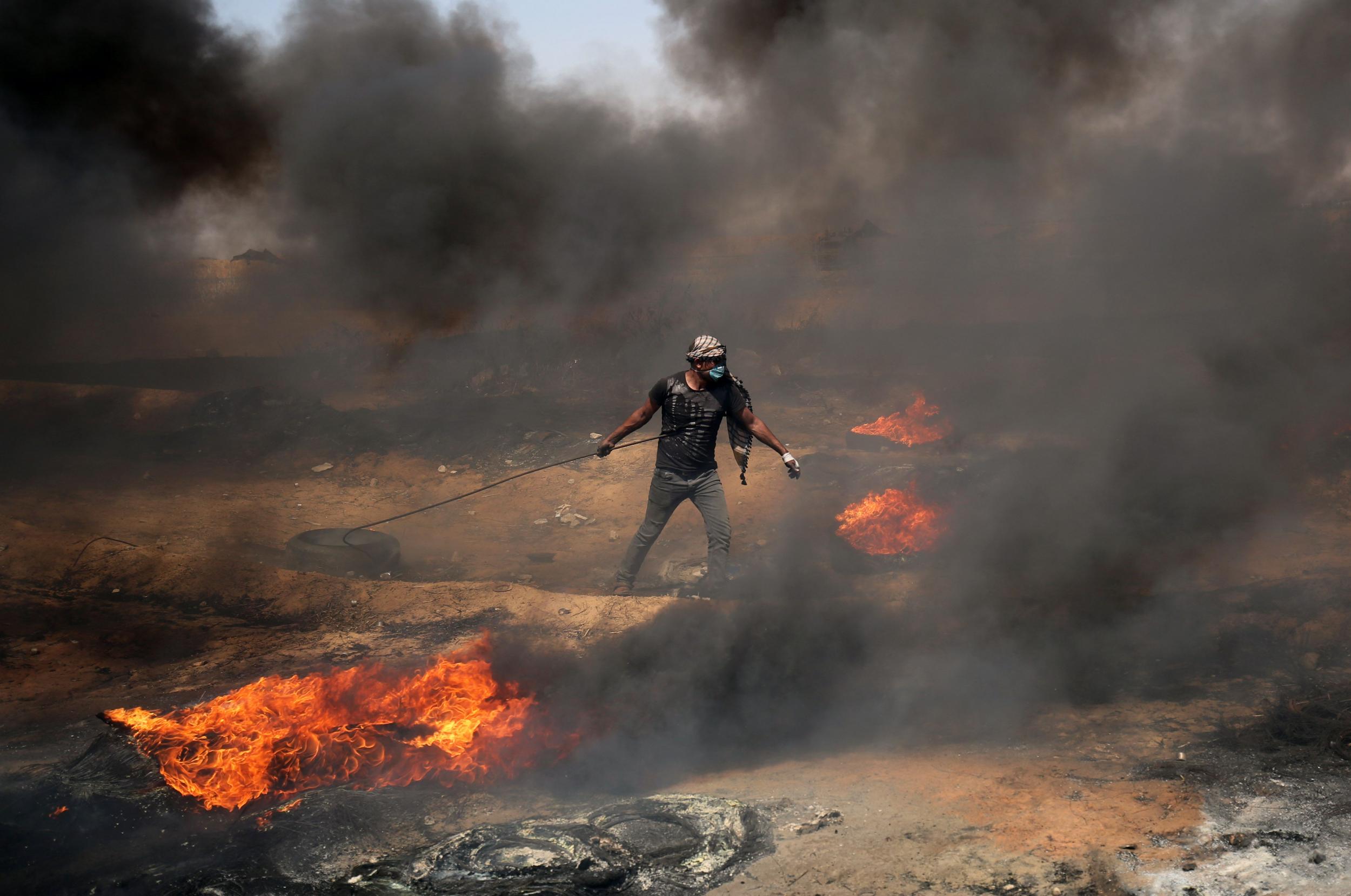 A Palestinian demonstrator moves a burning tyre during clashes with Israeli forces