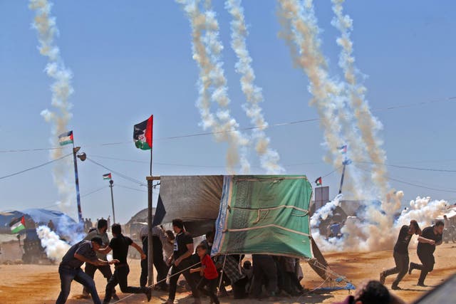 Palestinians run for cover from tear gas near the border between Israel and the Gaza Strip