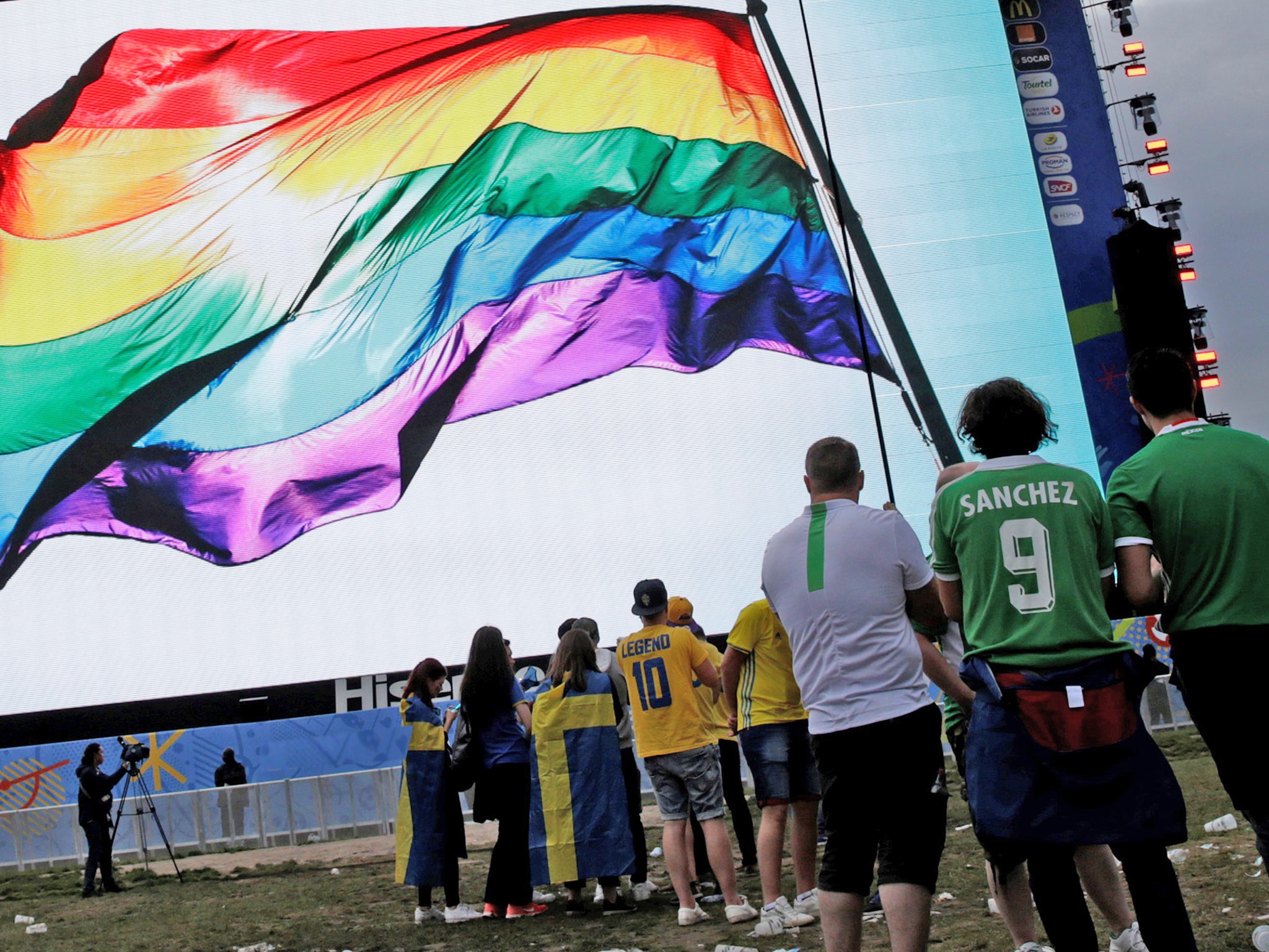 Football fans display a rainbow flag while watching a game