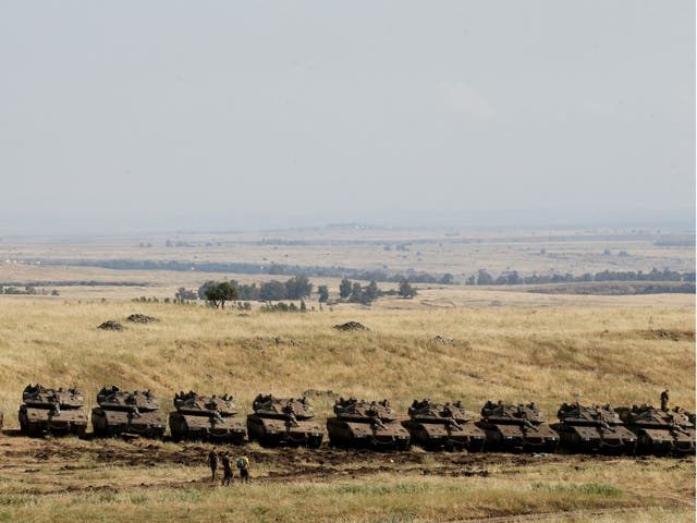 Israeli soldiers walk past tanks near the border with Syria in the Golan Heights