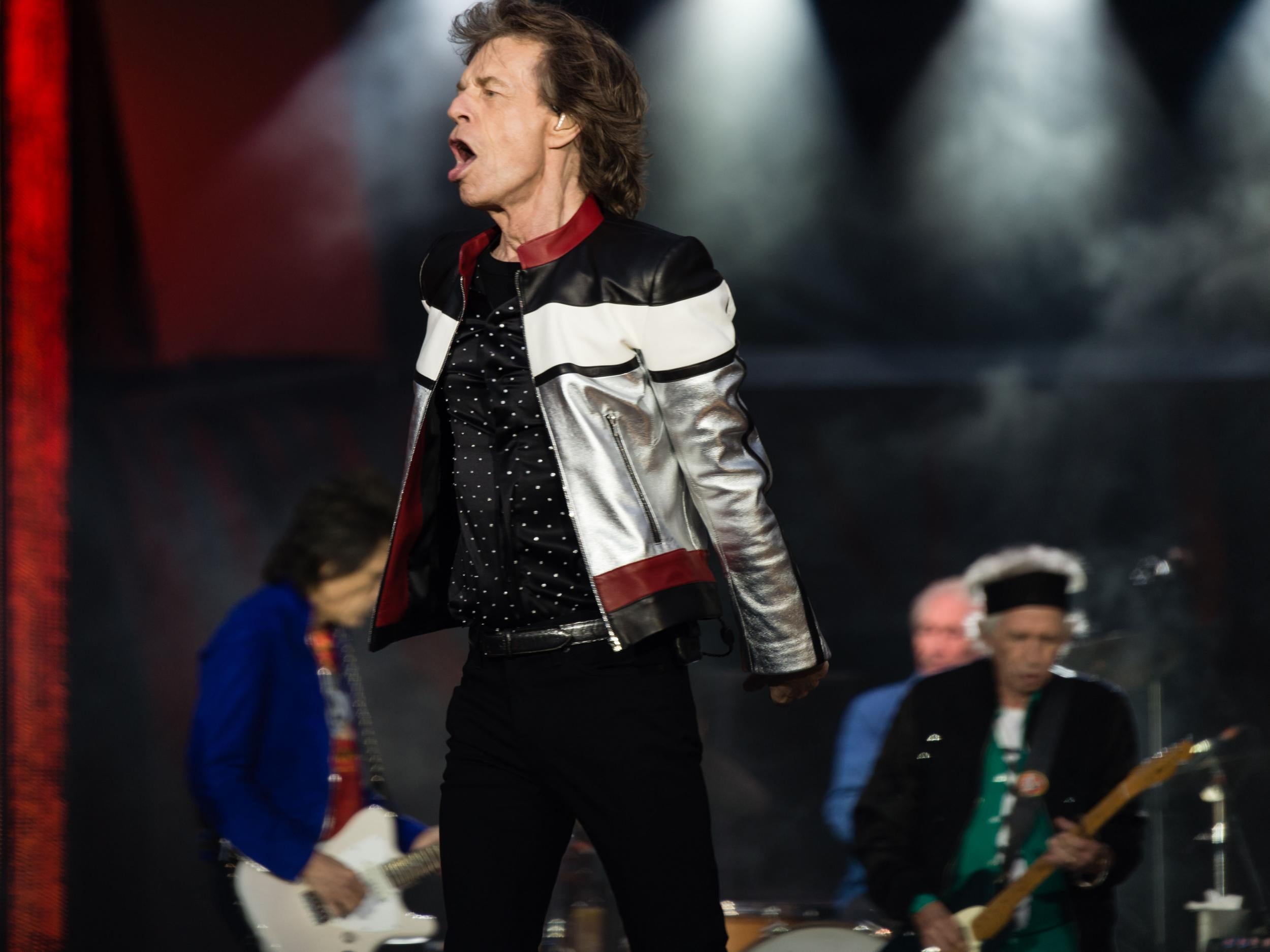 Mick Jagger is omnipresent, bursting on to the enormous stage in a silver, black and red jacket