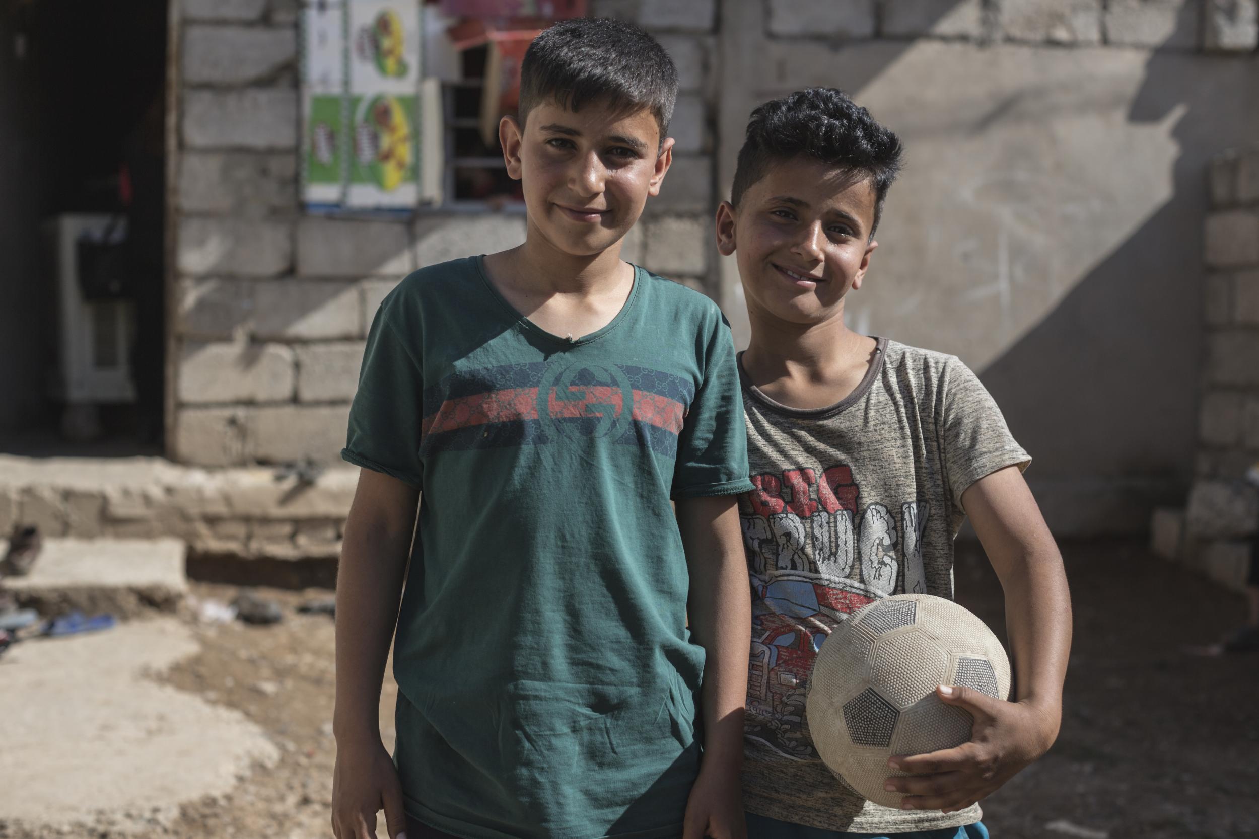 Nour, 12, stands with his 10-year-old brother Mahmoud (not their real names) in the yard outside their one-room house in West Mosul, Iraq, on 16 April 2018. As the eldest, Nour feels responsible for his siblings since his father died last year