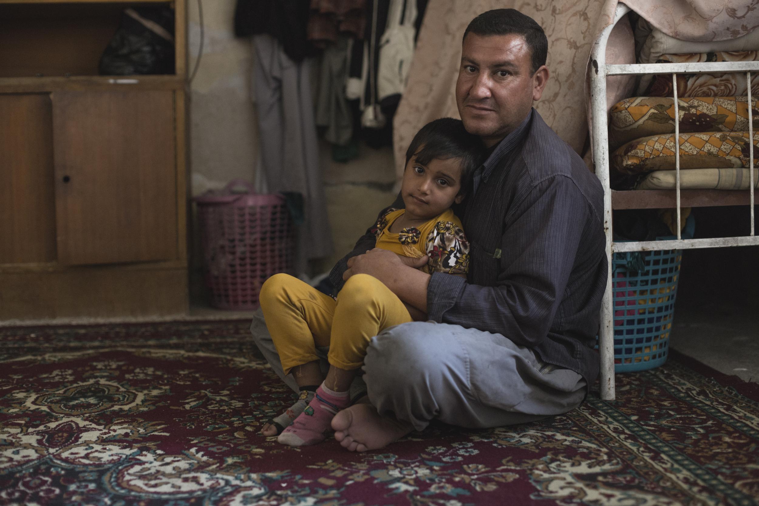 Six-year-old Thani (not her real name) sits with her father in their home in West Mosul?on 16 April 2018. The little girl watched her mother die after a mortar shell hit their home last year