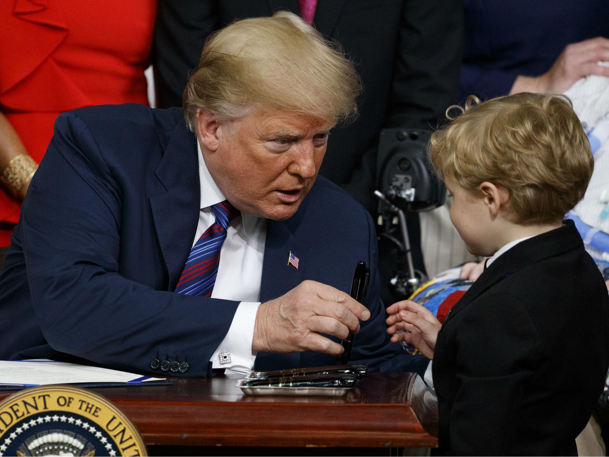 Mr Trump hands a pen to a child with muscular dystrophy after signing the right to try law