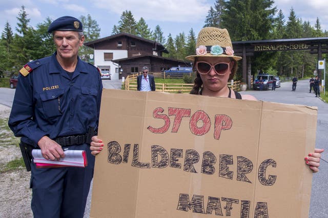 A woman holds a protest sign in front of a police checkpoint on a road leading to the Interalpen-Hotel Tirol, venue of the Bilderberg conference, on 12 June 2015 near Telfs, Austria