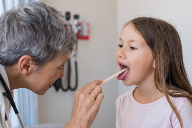 <p>A GP inspecting a child’s tonsils </p>
