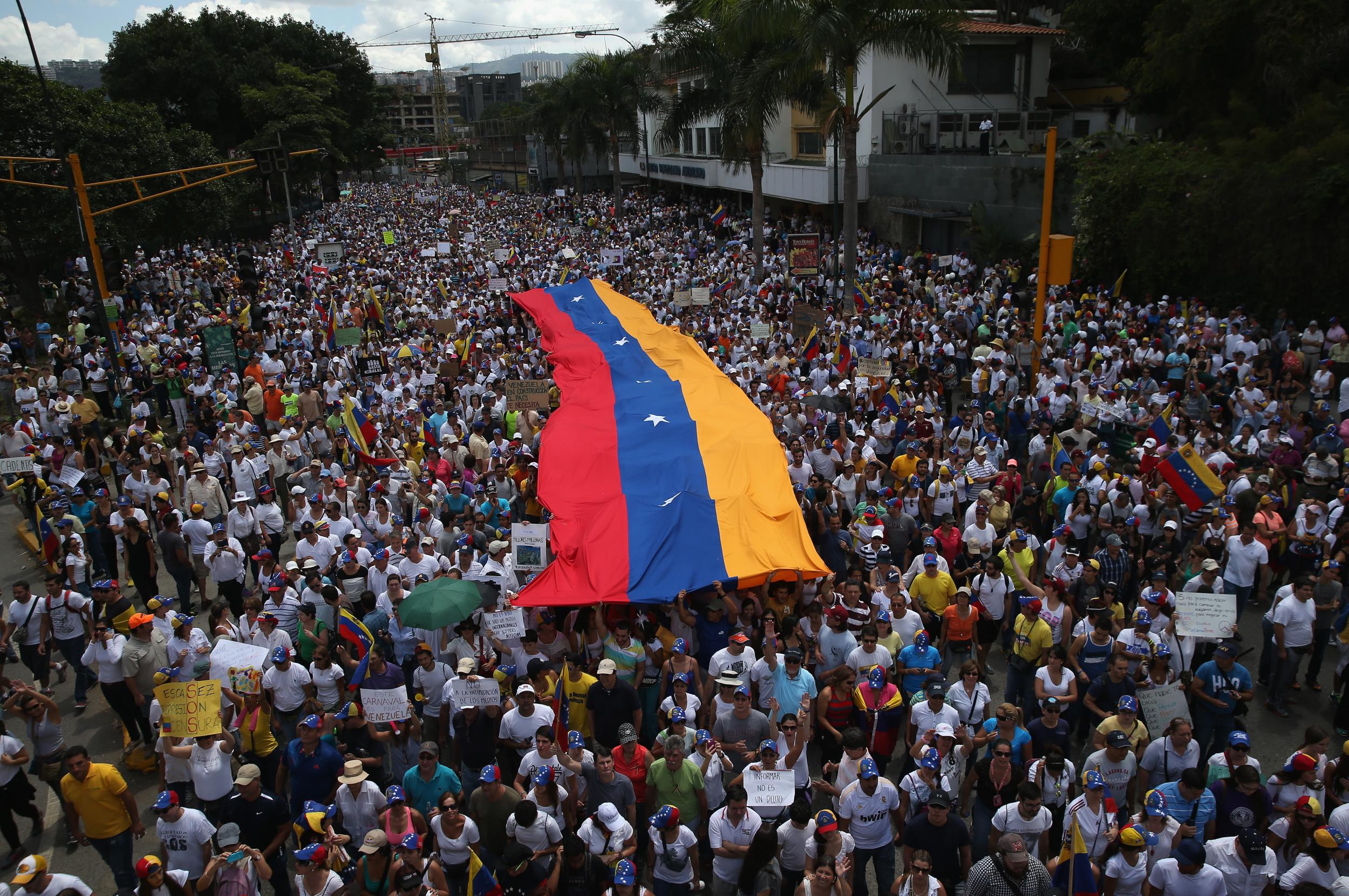 Carrying a giant Venezuelan flag, thousands of anti-government protesters march during a mass demonstration