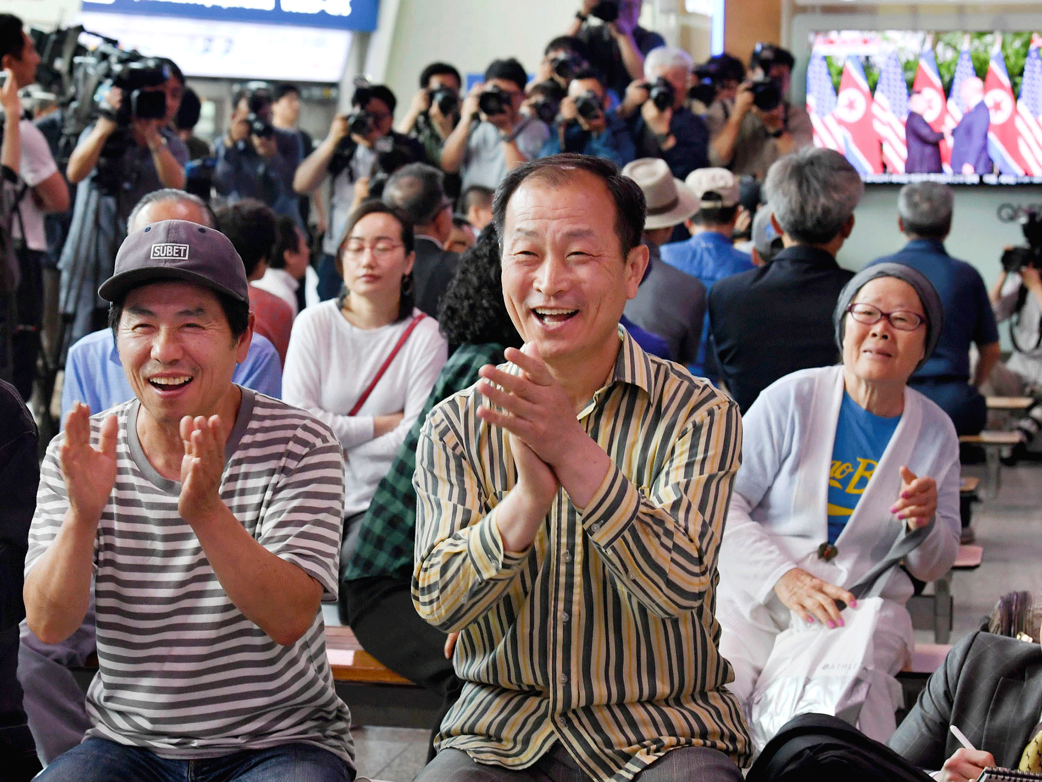 People celebrate as they watch a TV showing US President Donald Trump meets with North Korean leader Kim Jong Un at Seoul Railway Station in Seoul