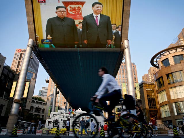 People bicycle past a giant TV screen broadcasting the meeting of visiting North Korean leader Kim Jong-un and Chinese president Xi Jinping