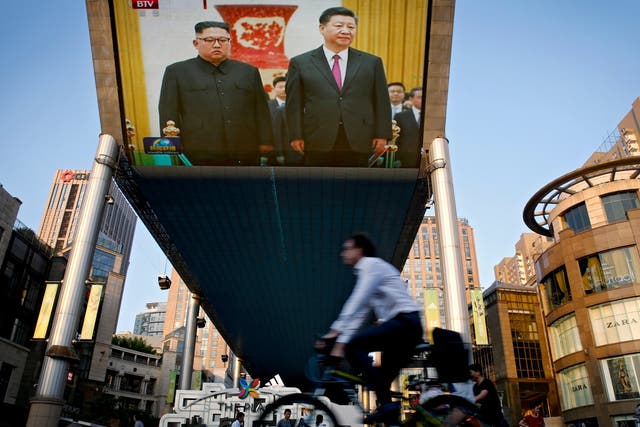 People bicycle past a giant TV screen broadcasting the meeting of visiting North Korean leader Kim Jong-un and Chinese president Xi Jinping