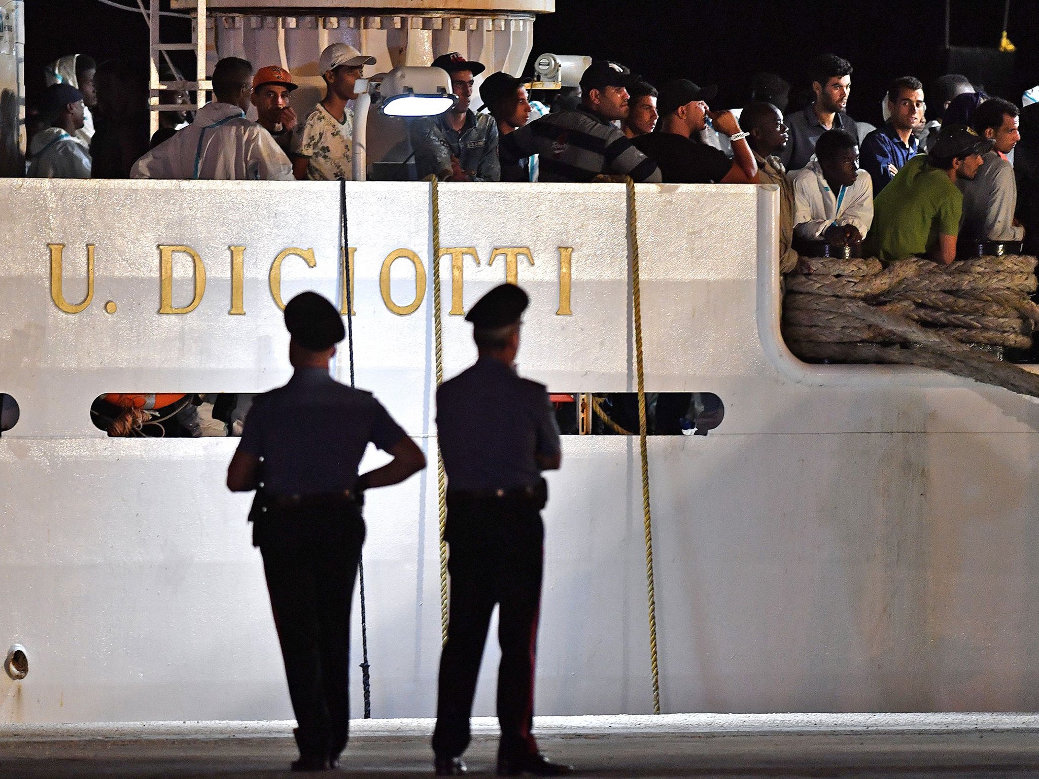Authorities watch over a boat containing refugees as it attempts to port in Sicily