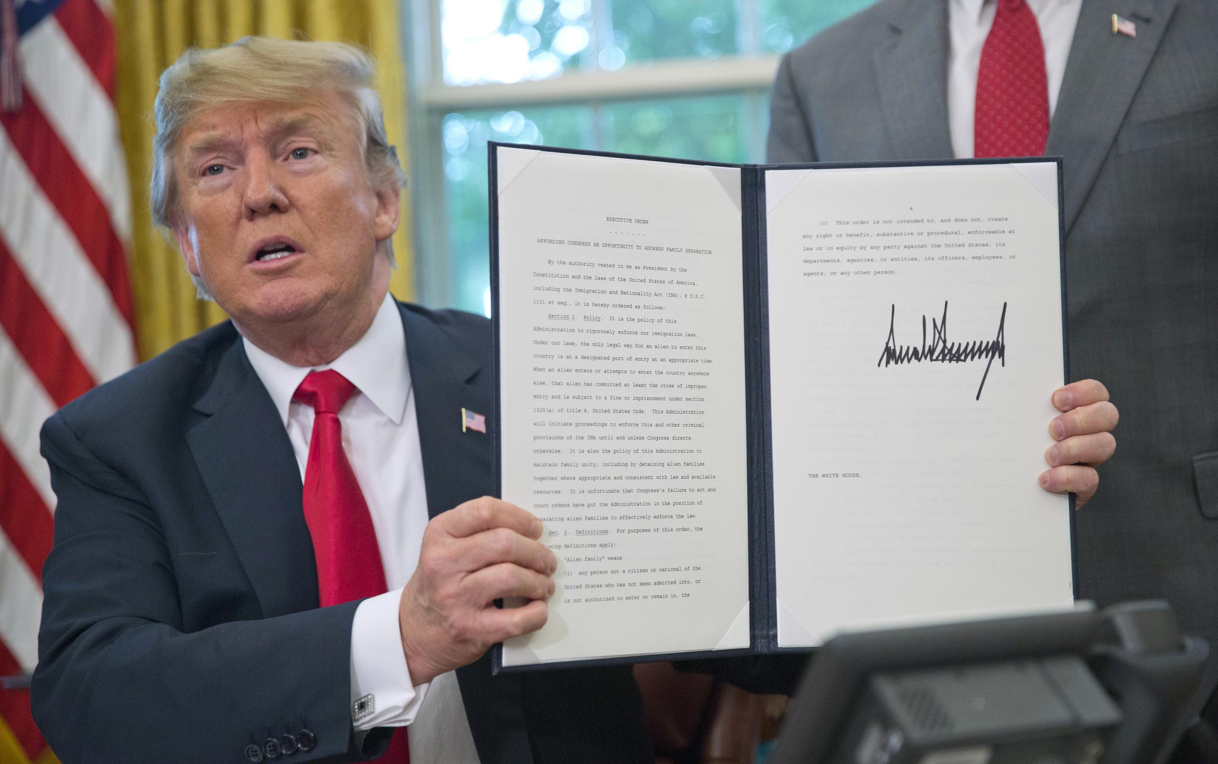 President Donald Trump holds up the executive order he signed to end family separations, during an event in the Oval Office