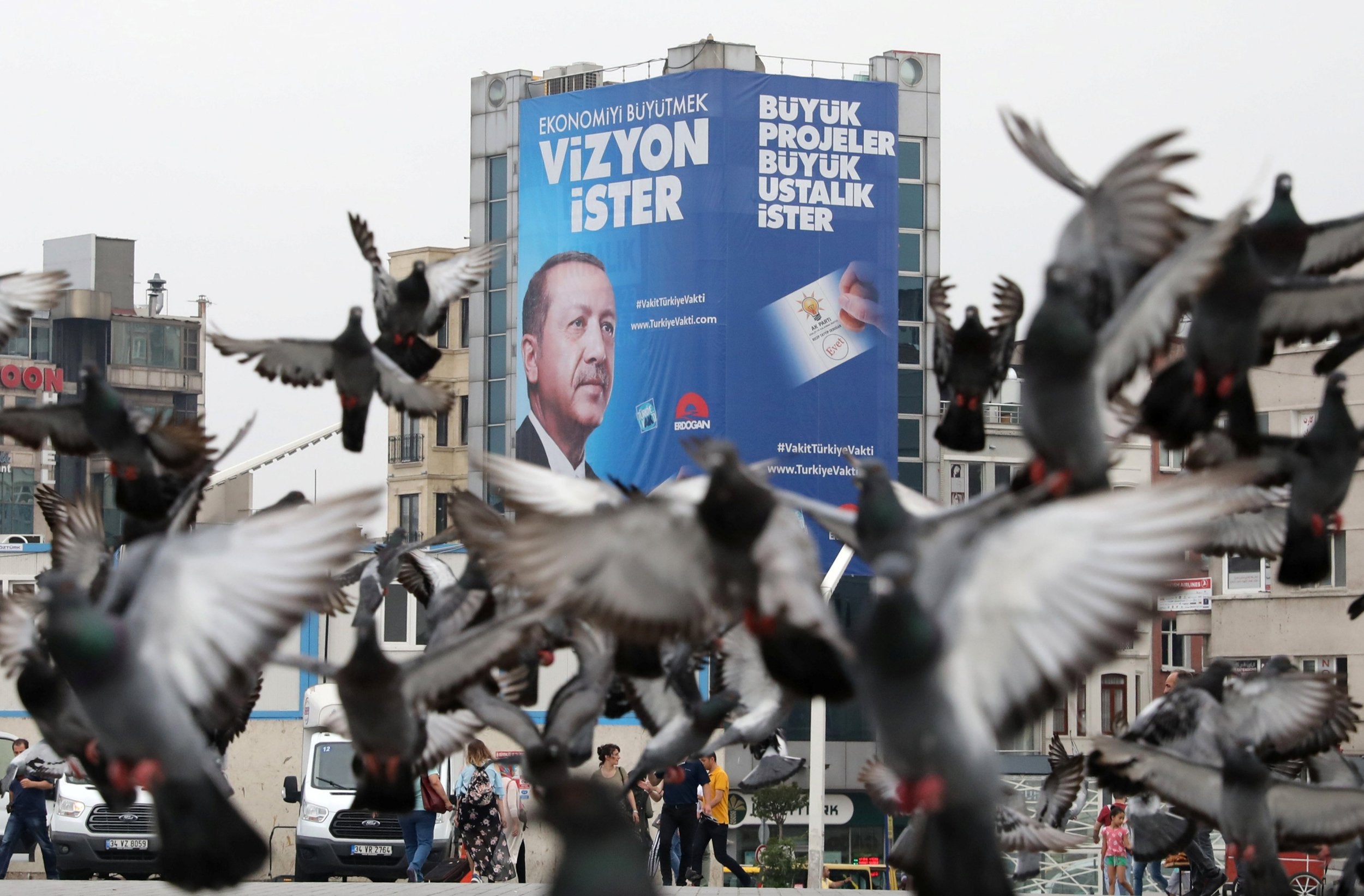 Pigeons fly in front of a large election poster of Turkish President Tayyip Erdogan in Istanbul